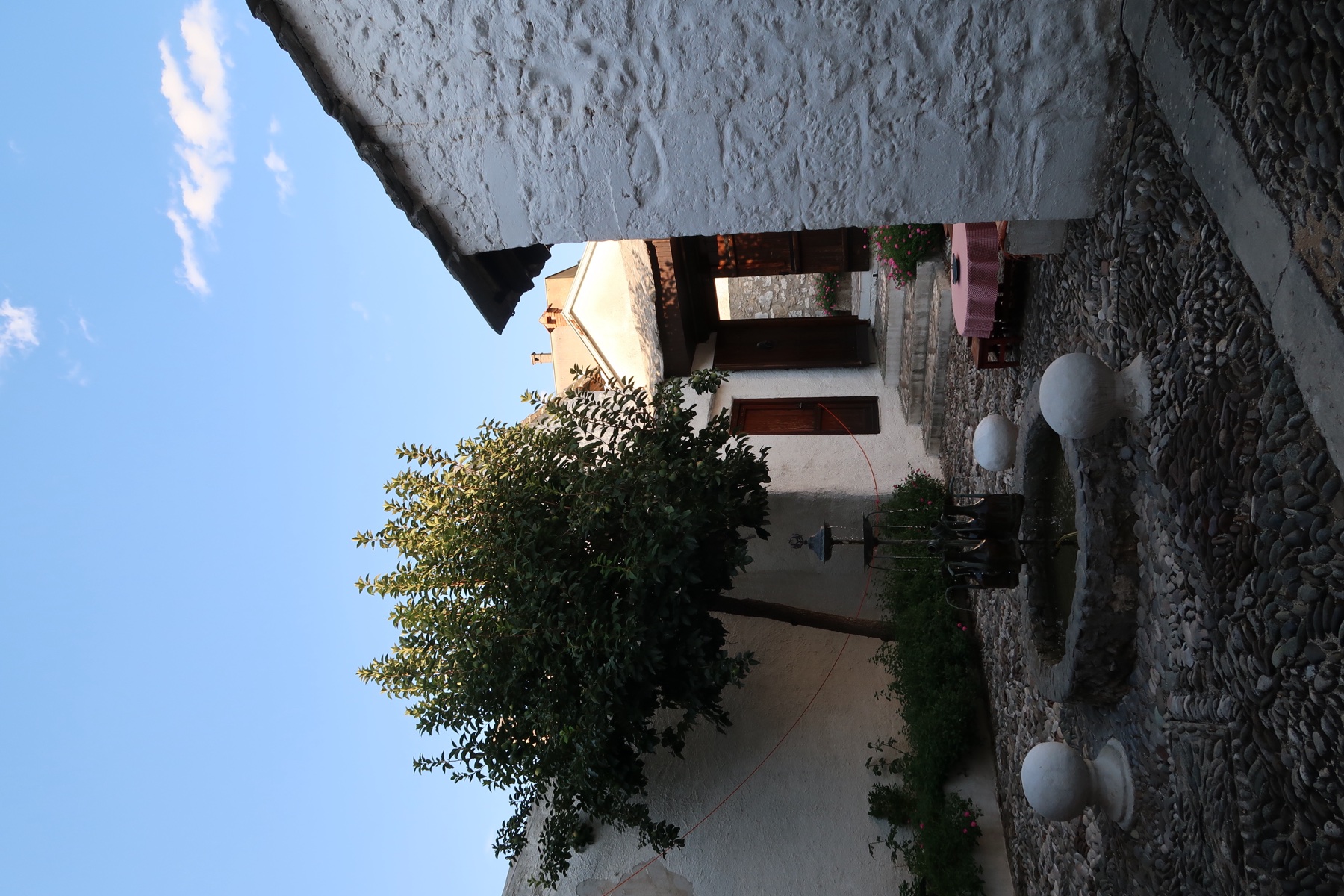 Whitewashed stone courtyard with a small fountain, a leafy tree and pebble paving
